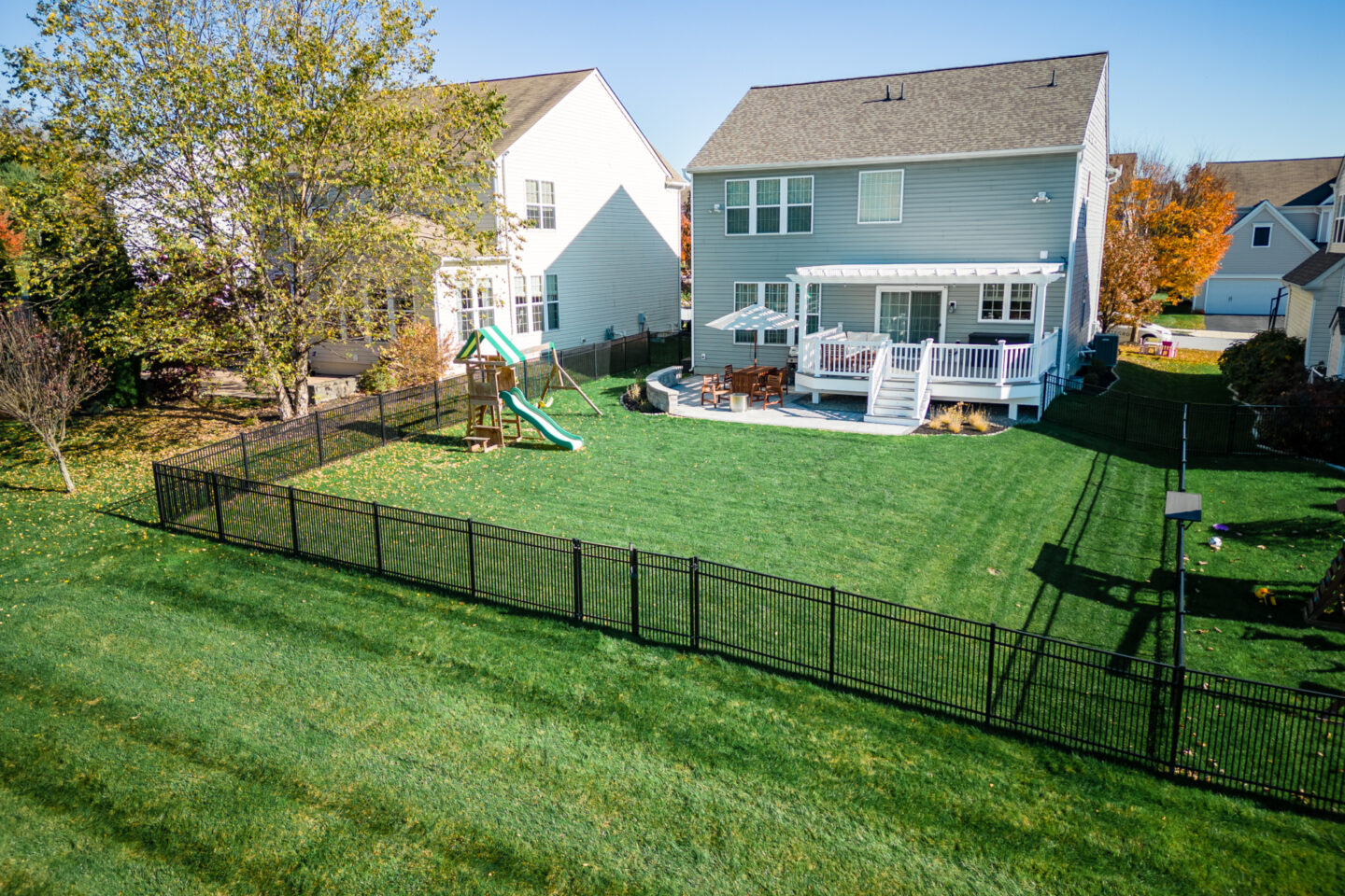 image of a deck and patio in downingtown pa built by integrous fences and decks featuring a white vinyl pergola timbertech decking white vinyl railing paver patio and sitting wall around the yard is a black aluminum fence