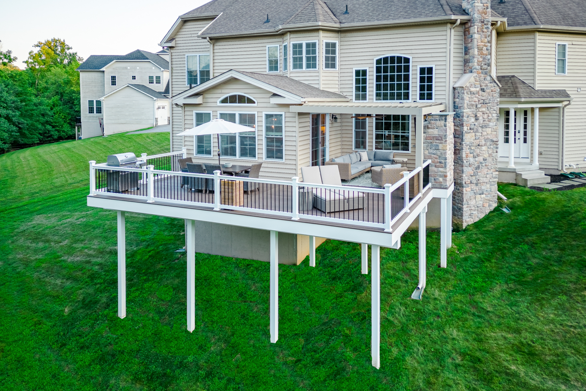 image of a deck with a equinox pergola a stone fireplace and vynl railing with aluminum balusters built by integrous fences and decks